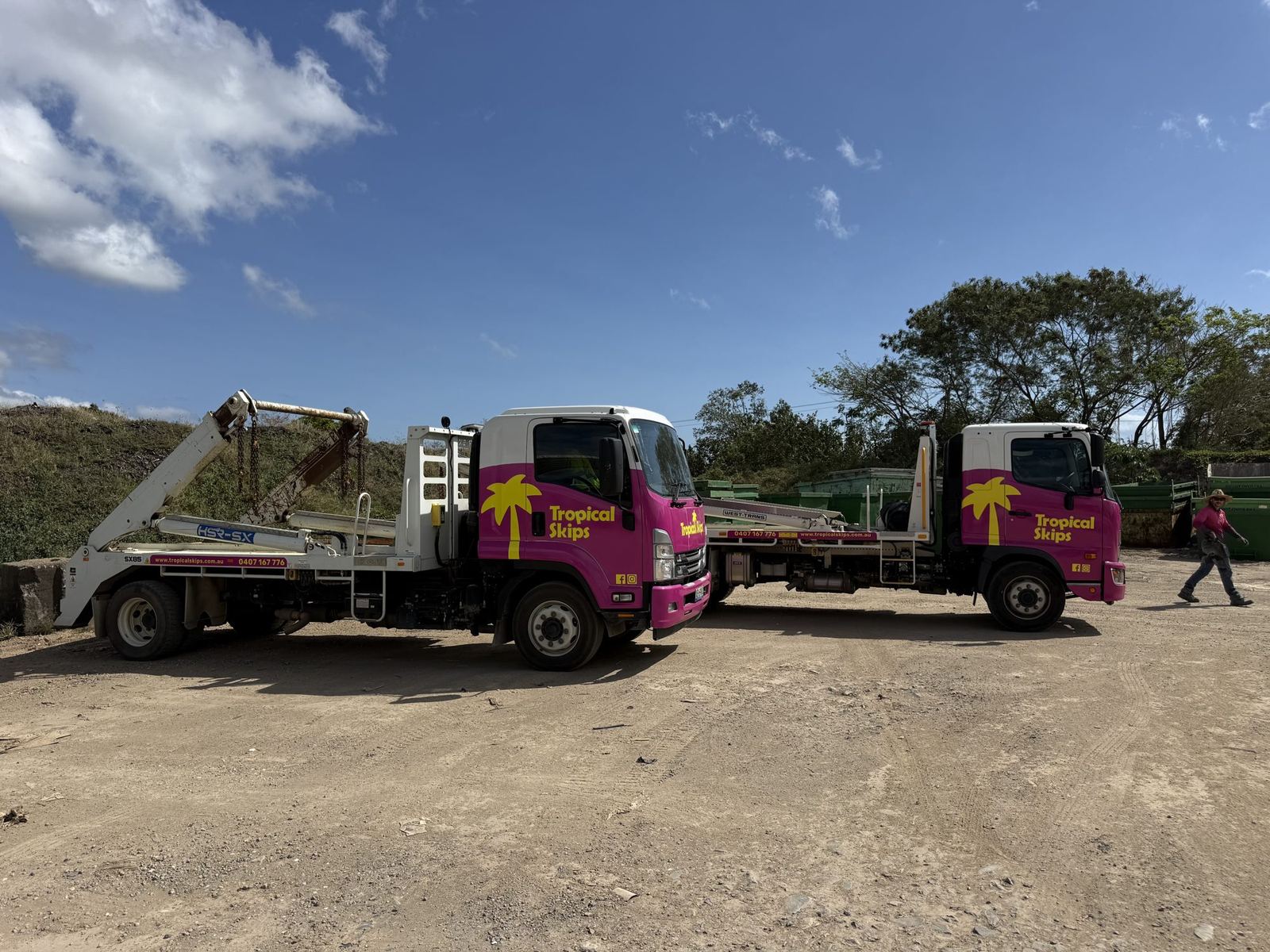 Two Tropical Skips trucks at the yard with a team member standing between them