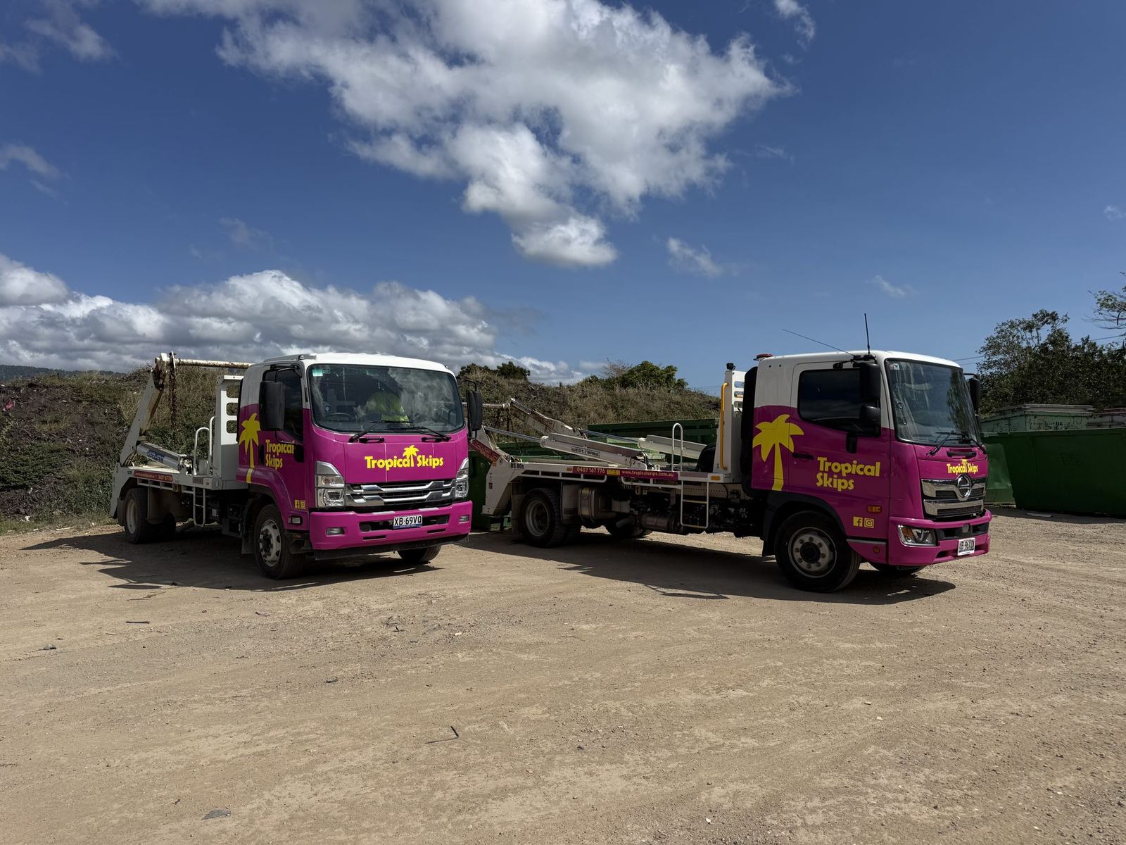 Two Tropical Skips trucks with their lift arms raised at the yard